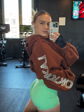 Load image into Gallery viewer, Brown Boyfriend Hoodie with silver rhinestone sleeve lettering, worn in a gym
